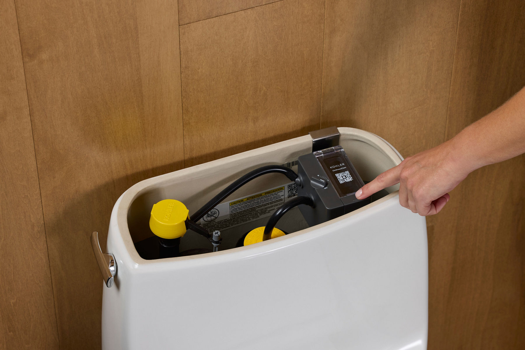 Person interacting with a Kohler smart toilet tank component, featuring a QR code for setup or troubleshooting.