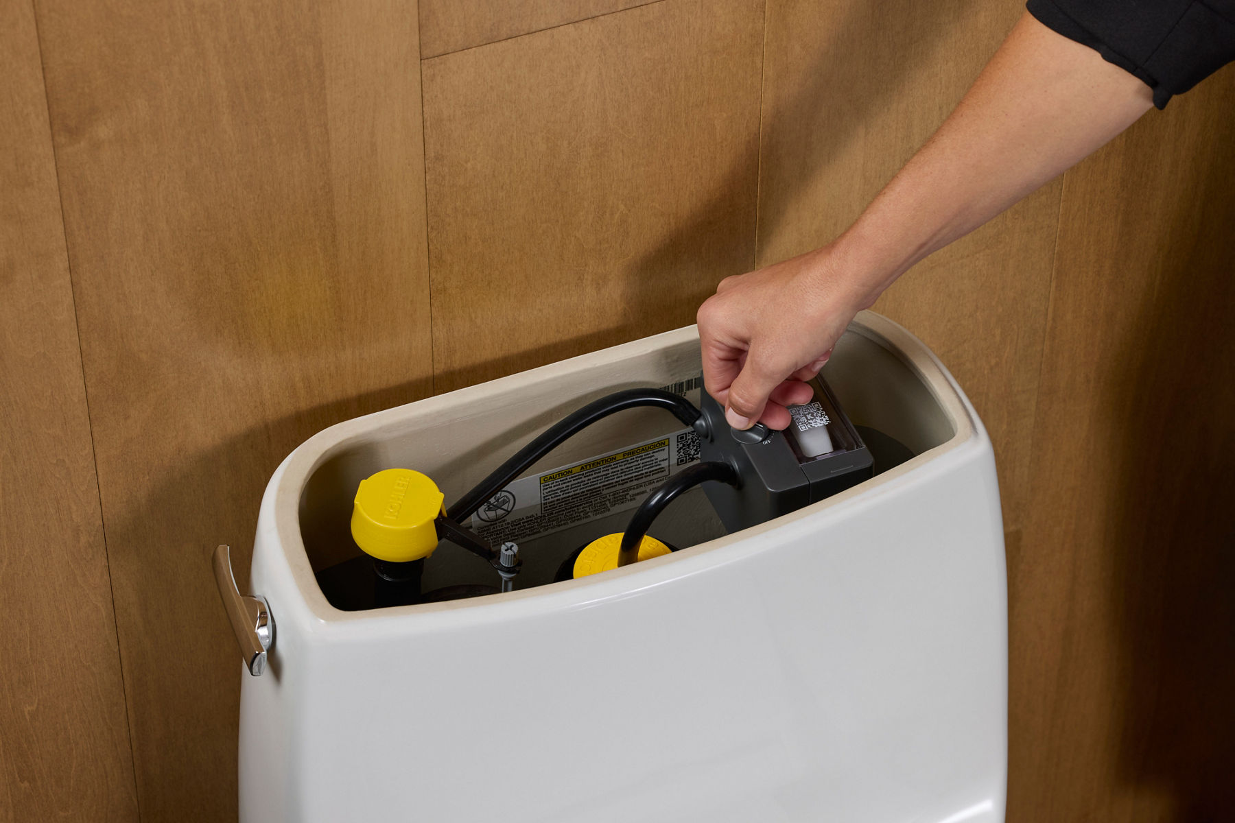Person adjusting a component inside the tank of a Kohler smart toilet for customization or maintenance.