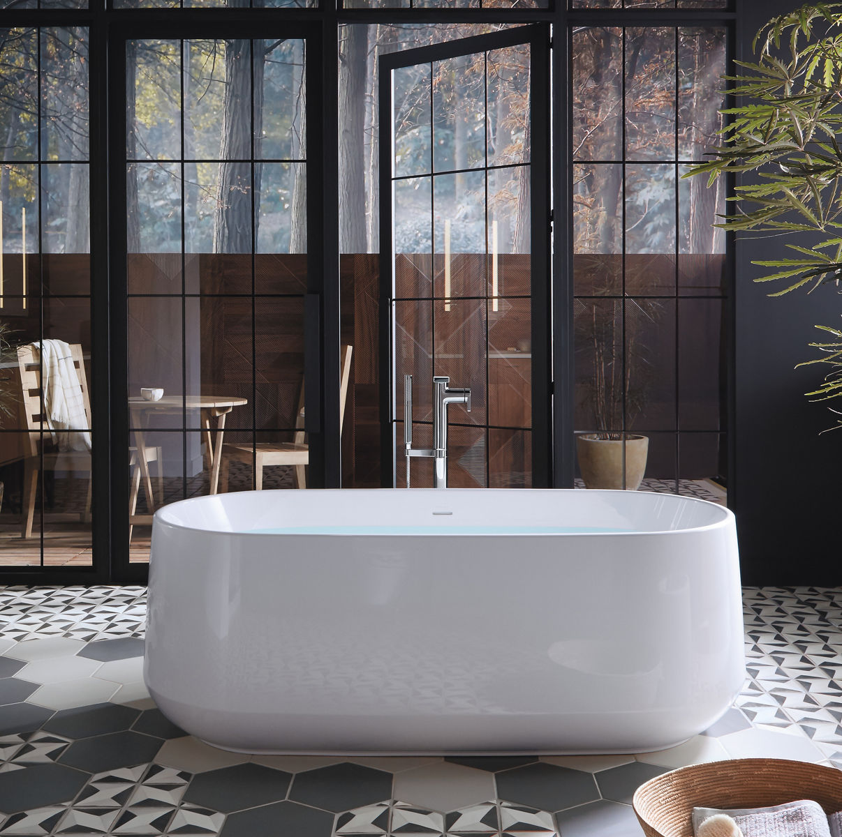 A white KOHLER Ceric freestanding bath with Composed floor mount bath filler stands before glass doors leading onto a balcony with a table and chairs.