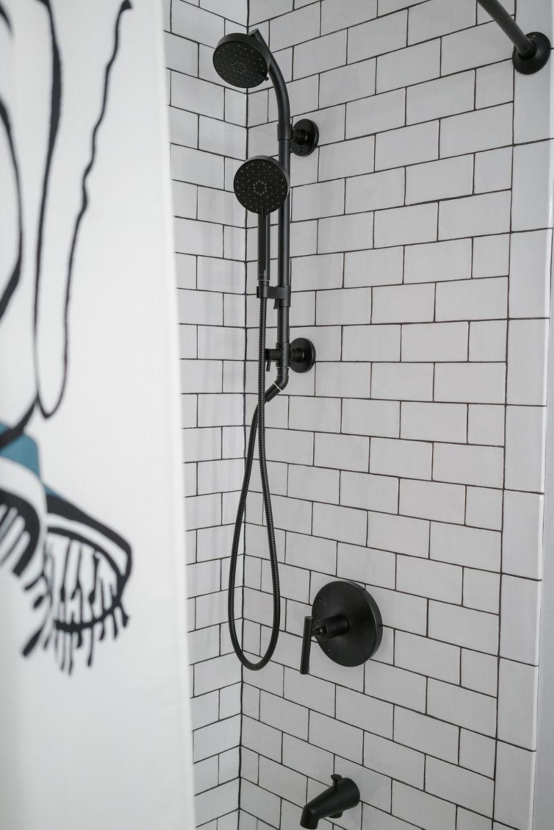Black and white close up of bathroom shower at the Saint Kate hotel featuring KOHLER Matte Black shower and bathroom accessories.