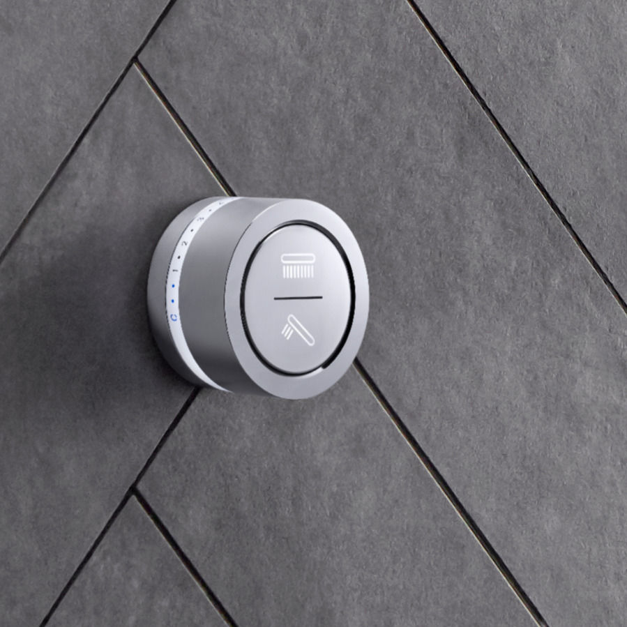 Gros plan de l’interface de douche en mode DTV de KOHLER en chrome poli installée sur un mur de douche carrelé en pierre grise.