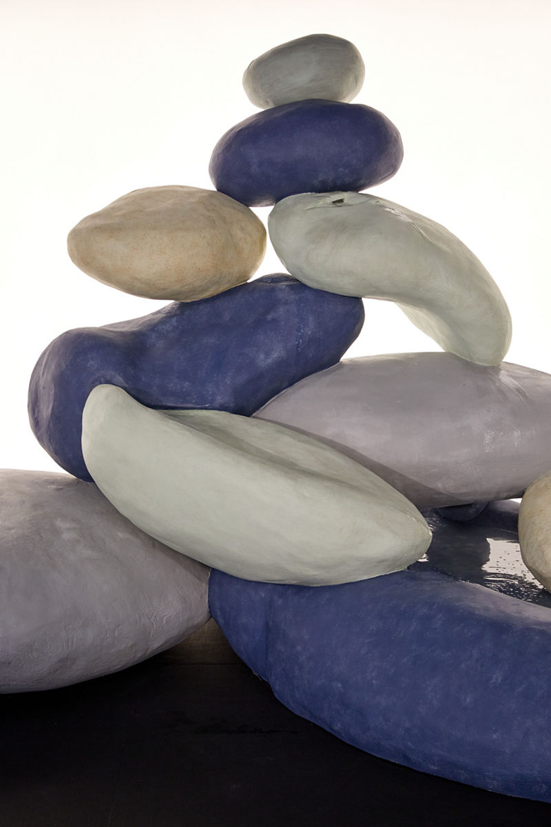 Une sculpture de gros objets violets, verts, gris et blanc cassé semblables à des pierres disposés dans une pile. La sculpture contient environ 10 objets et mesure environ 8 pieds de haut.