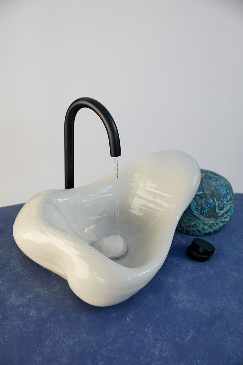 Un évier Rock.01 et un robinet noir mat posés sur une grande sculpture violette en forme de pierre.