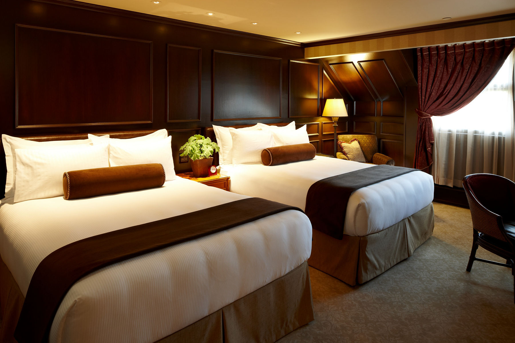 An elegant suite at the American Club with dark wooden walls and double-beds.