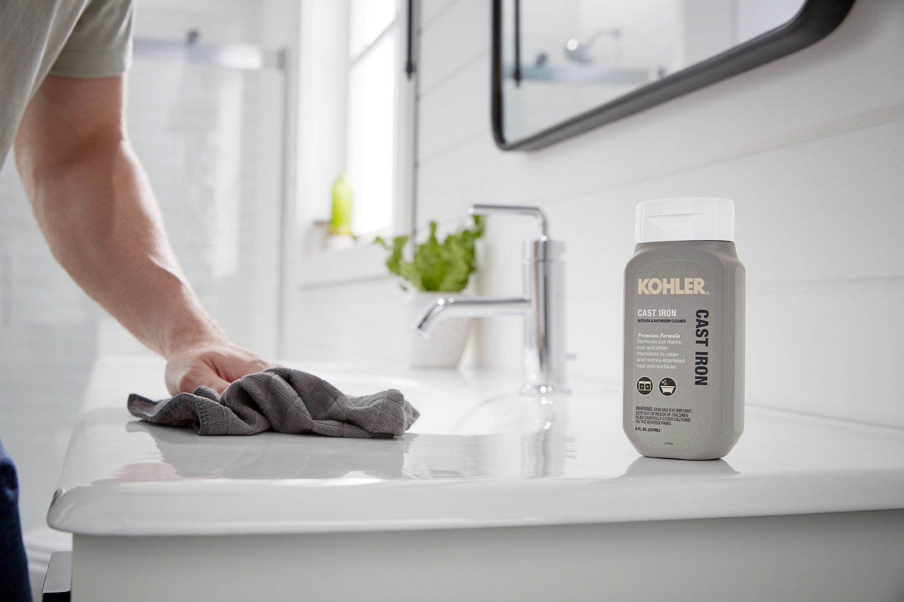 Un homme nettoie un lavabo de salle de bain en fonte avec un produit de nettoyage en fonte KOHLER
