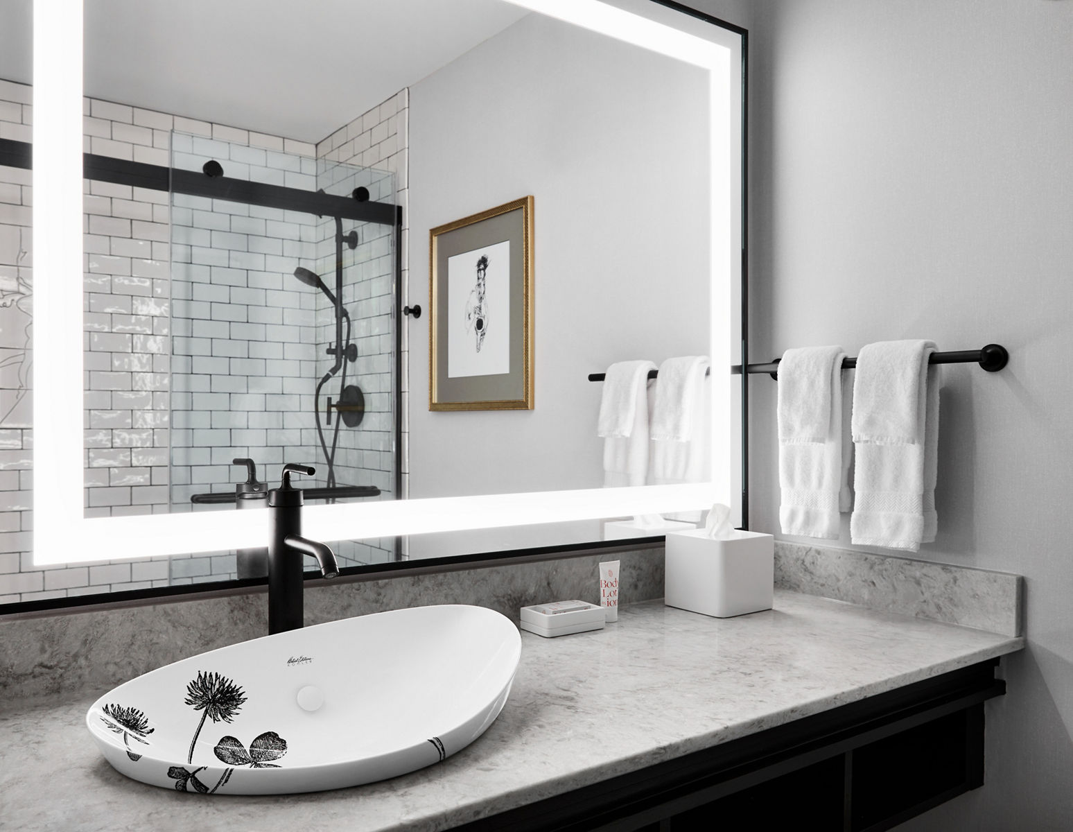 Black and white photo of contemporary bathroom with luminated vanity and Kohler’s Artist Editions™ handmade sink.