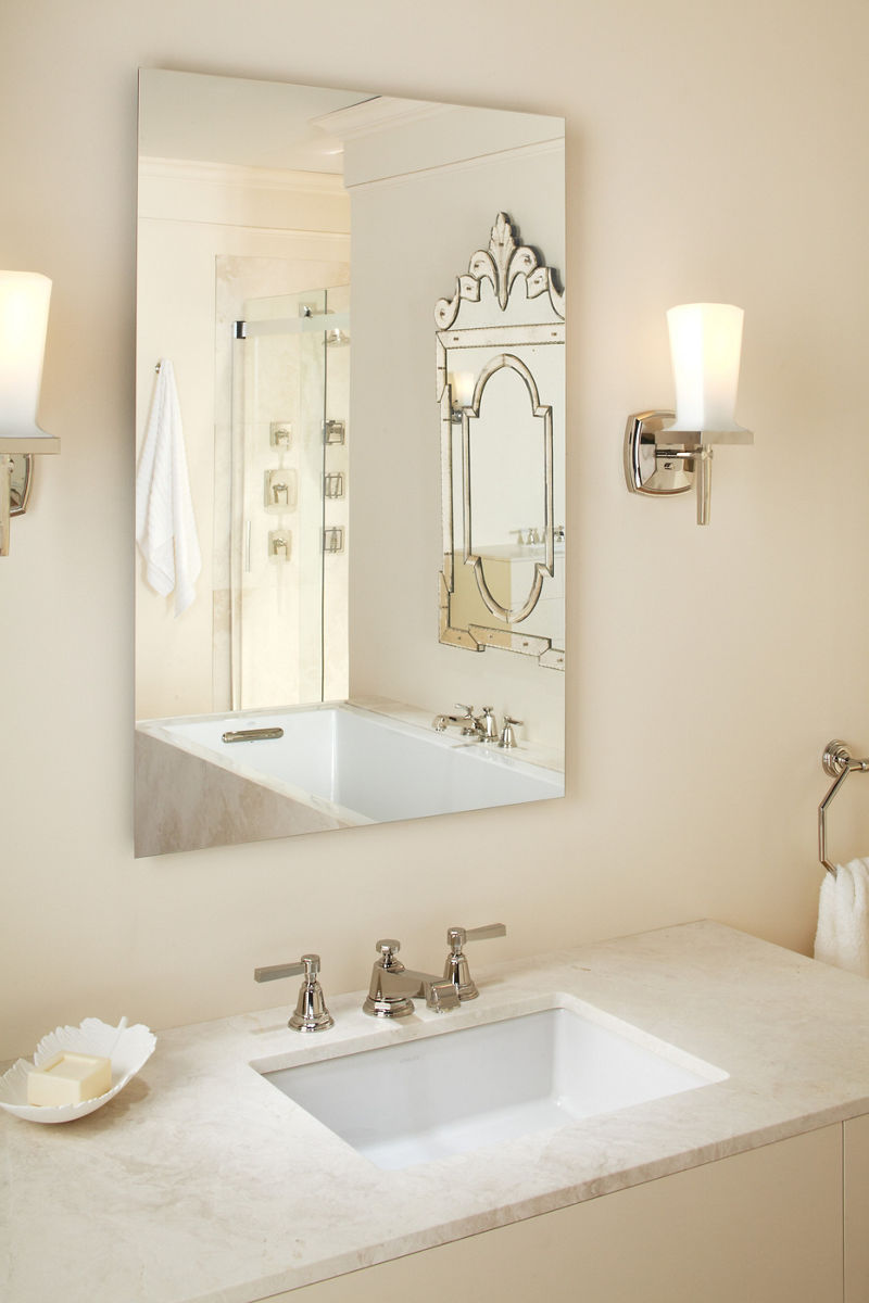 Un grand miroir de salle de bain sans cadre KOHLER est monté au-dessus d’un meuble-lavabo blanc avec un lavabo en sous-surface.