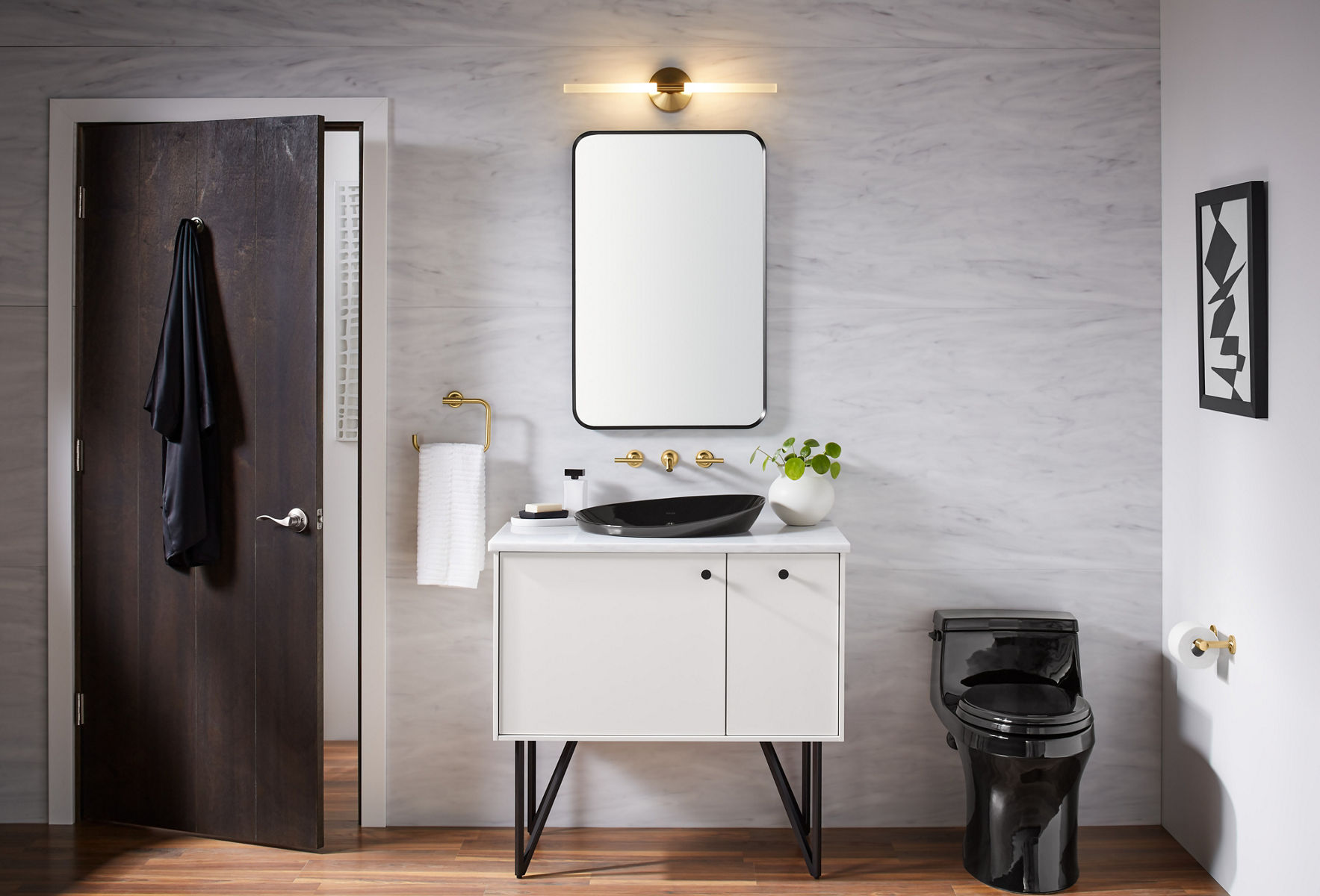 A bathroom with a black toilet on the right, vanity and mirror space in the center and a door on the left. The vanity and mirror have dotted lines illustrated over them horizontally and vertically to indicate the act of measuring the space.