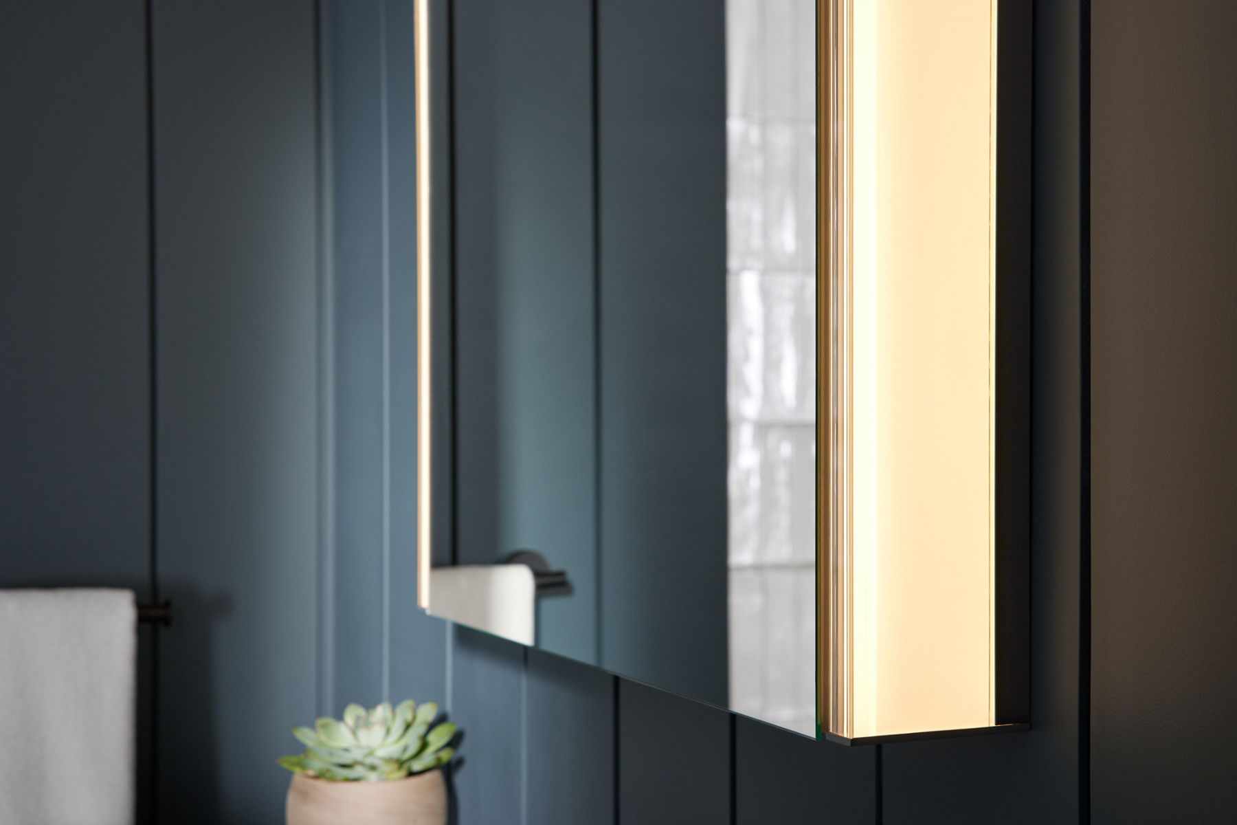 Side view of surface-mount medicine cabinet with a lighted side against a dark gray paneled wall. 