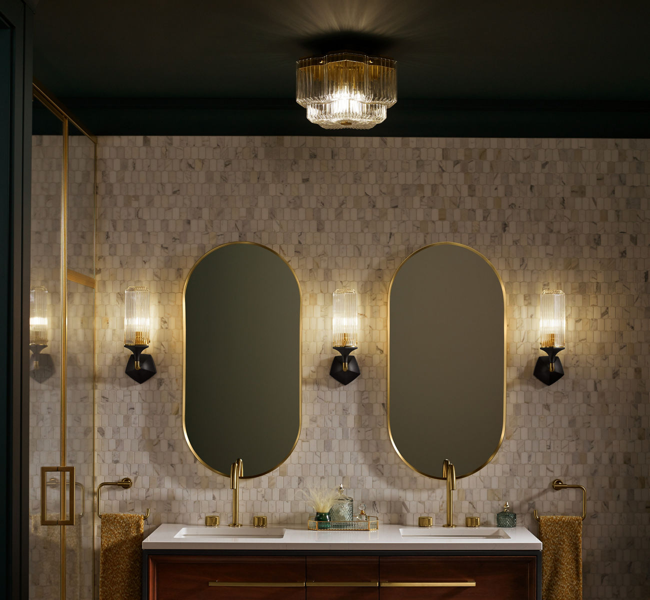 Deux miroirs en forme de capsule KOHLER à cadre en laiton et trois appliques au murs sur un mur carré carrelé blanc et havane.