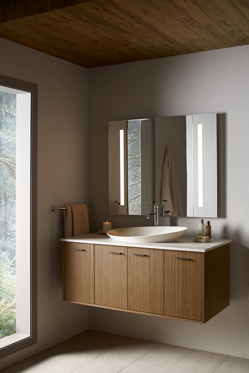 Un miroir éclairé Verdera de KOHLER projette même la lumière sur un meuble-lavabo au mur avec dessus blanc, robinet à poignée unique et lavabo de piscine ovale.