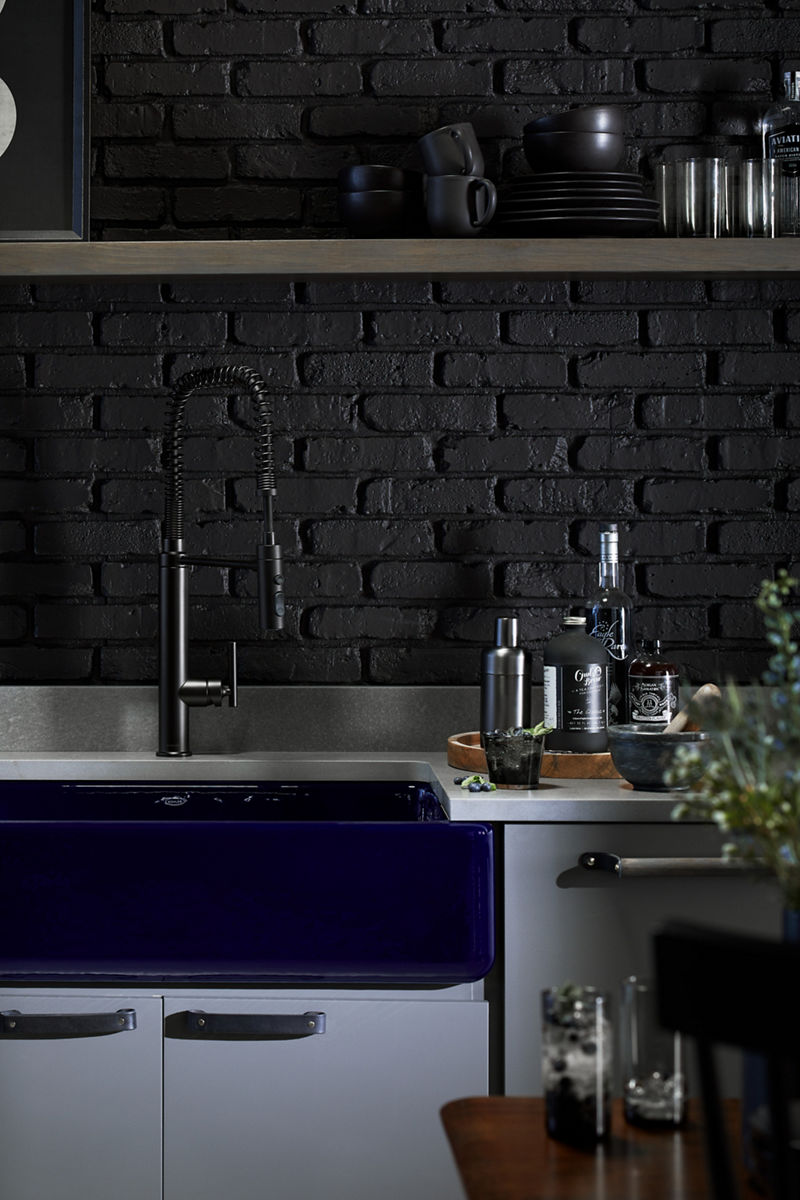 Un plateau avec des bouteilles de liqueur et un agitateur à cocktail repose sur un comptoir à côté d’un évier de style champêtre Whitehaven de KOHLER en bleu indigo.
