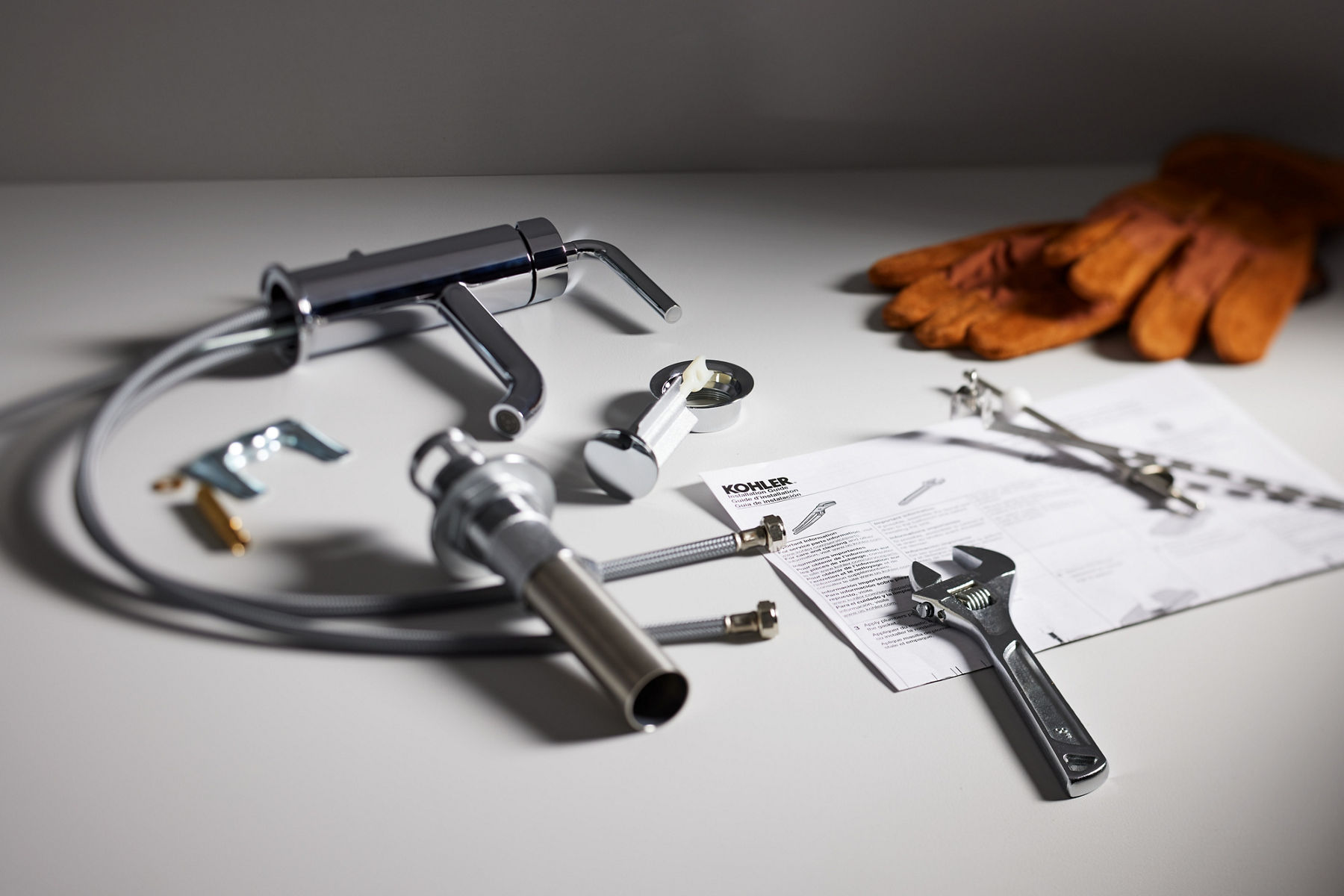 A selection of tools, hardware, and product insatllation instructions sit on a white counter, next to a pair of work gloves.