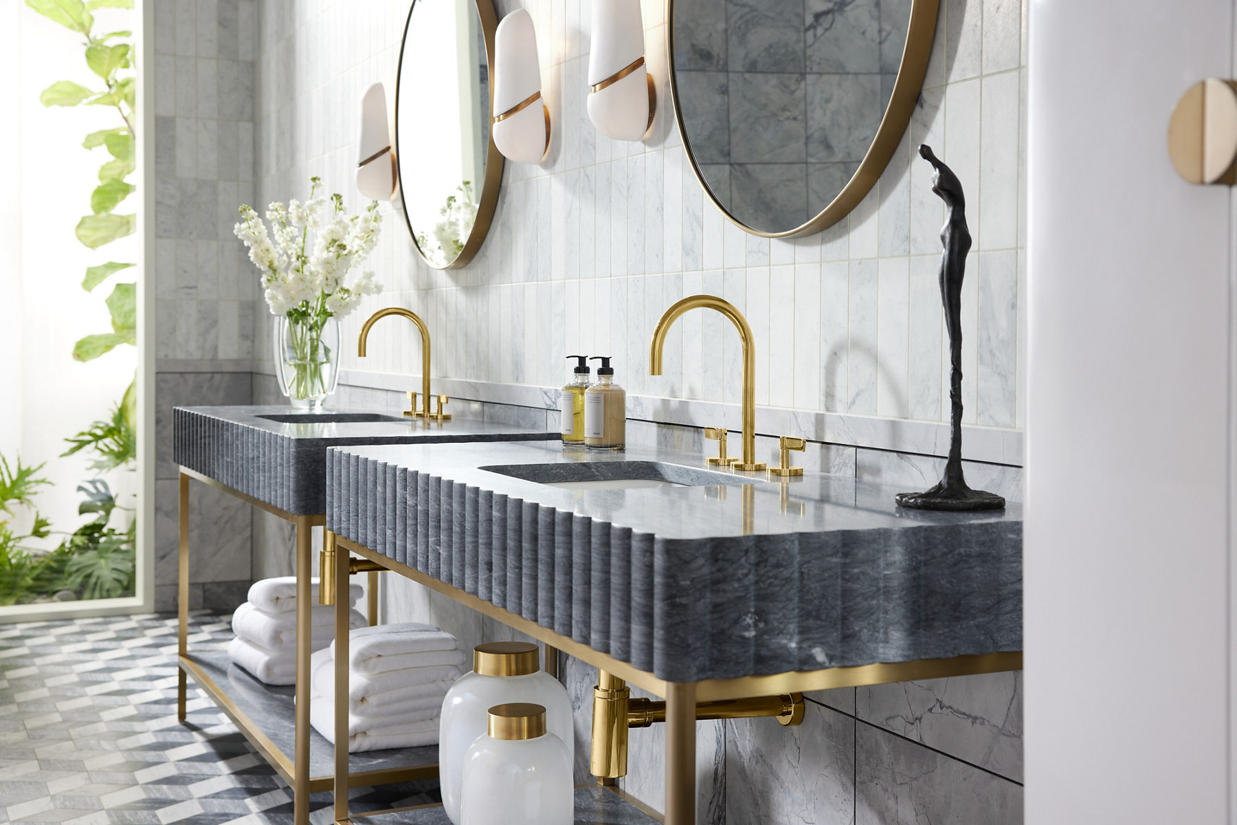 Two single bluish gray stone console table vanities with brushed brass legs and faucets.