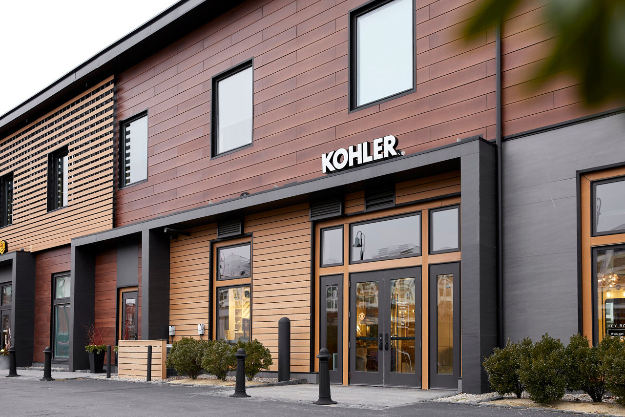 The outside entryway of a Kohler Signature Store, consisting of wood siding and black doors.