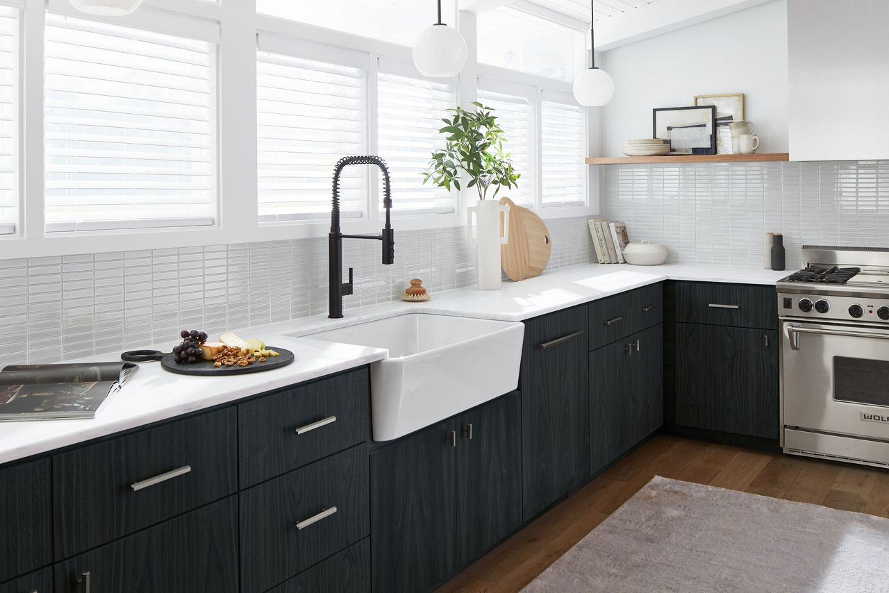 White countertops and a white KOHLER farmhouse sink contrast with black cabinets and a black single pull-out faucet with lever handle.