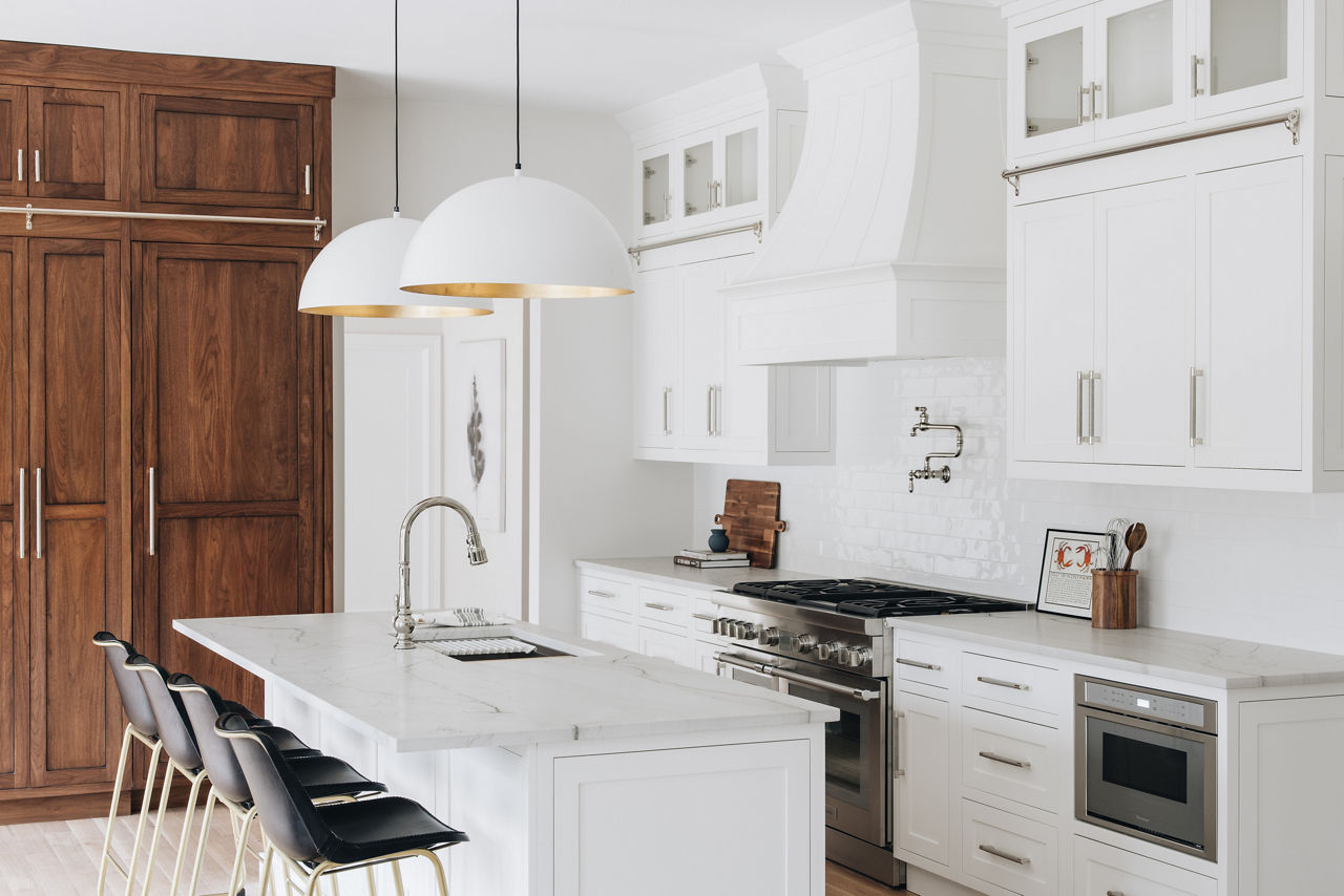 Wood doors and four black bar stools provide contrast in a white kitchen with island sink, KOHLER Artifacts touchless faucet, and Artifacts pot filler faucet.