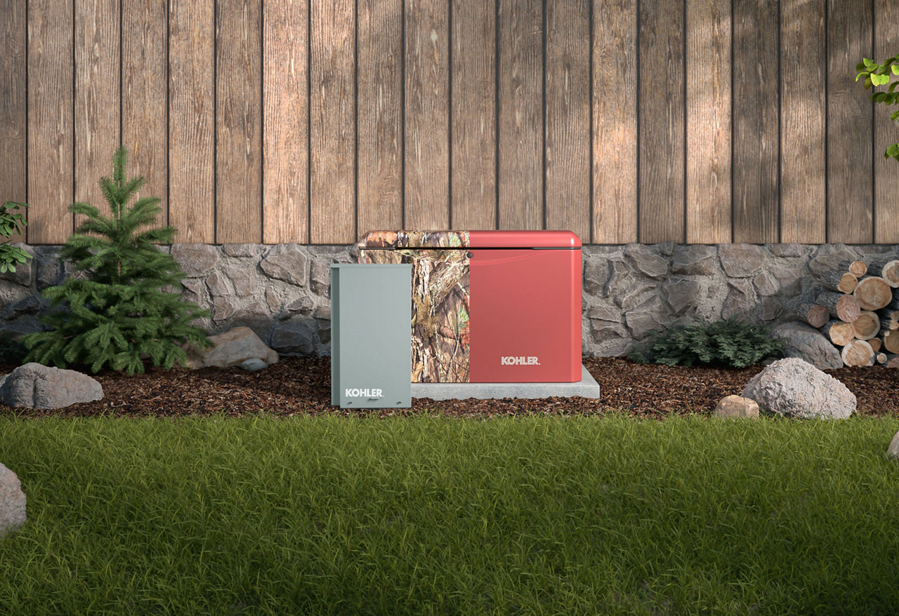 A generator half in camouflage and half in brick dust color with a control panel in front of it in an outdoor scene with a stone and wood fence.