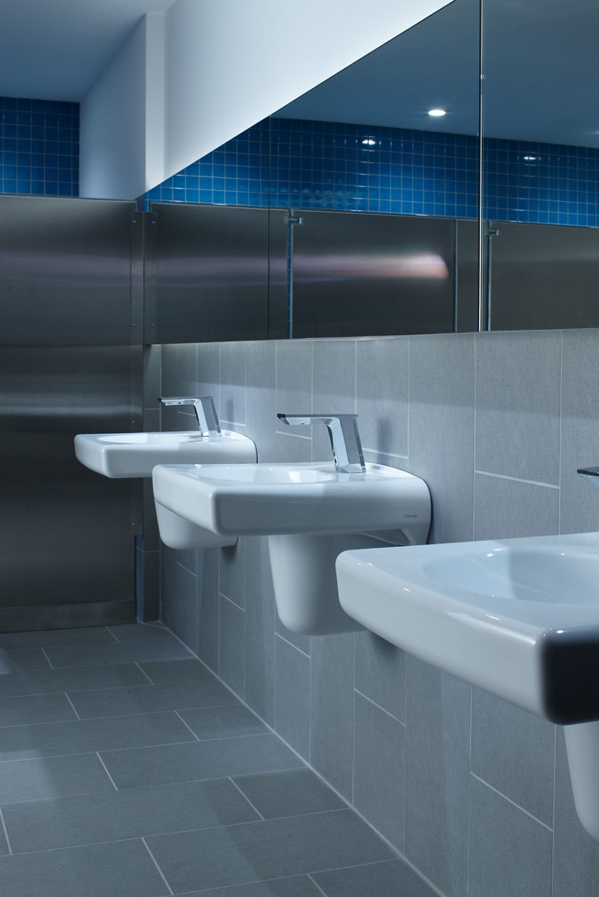 A row of white KOHLER Brenham wall-mounted commercial sinks with Polished Chrome single-hole Touchless faucets.