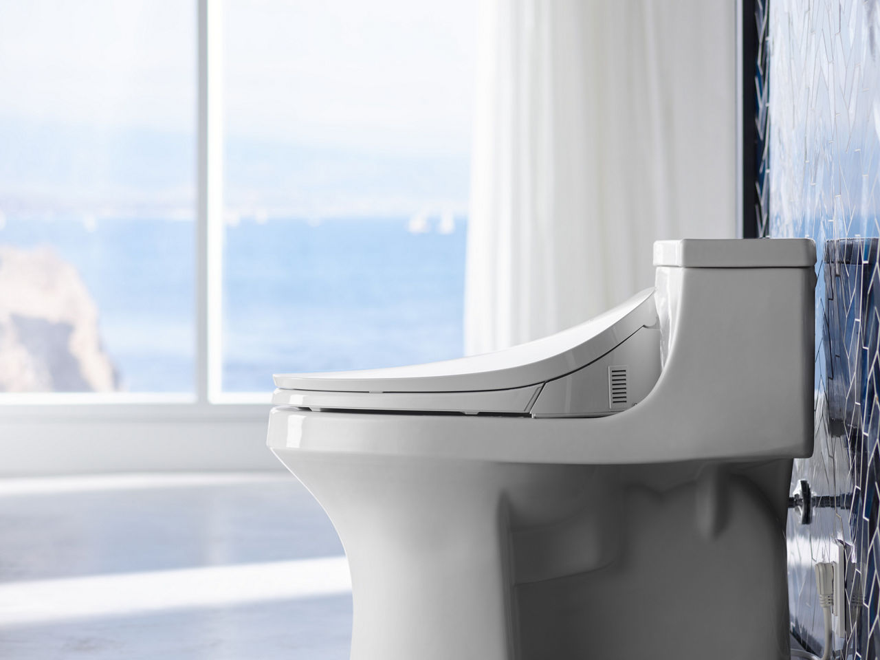 A side-view of a white KOHLER Sans Souci elongated toilet with C3 4-230 cleansing toilet seat.