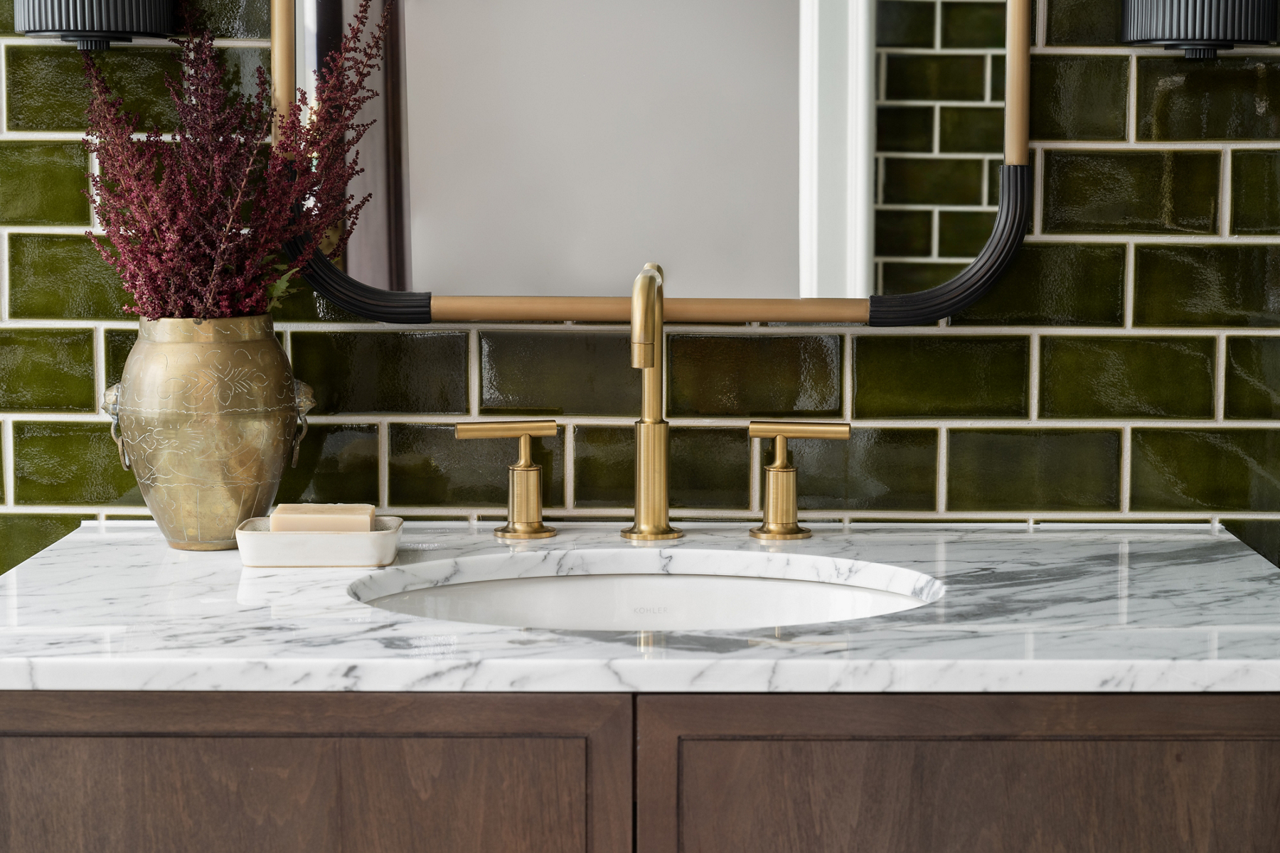 A close up shot of a bathroom sink with a white sink rounded bowl and gold faucet and handles all attached on the marble counter top.