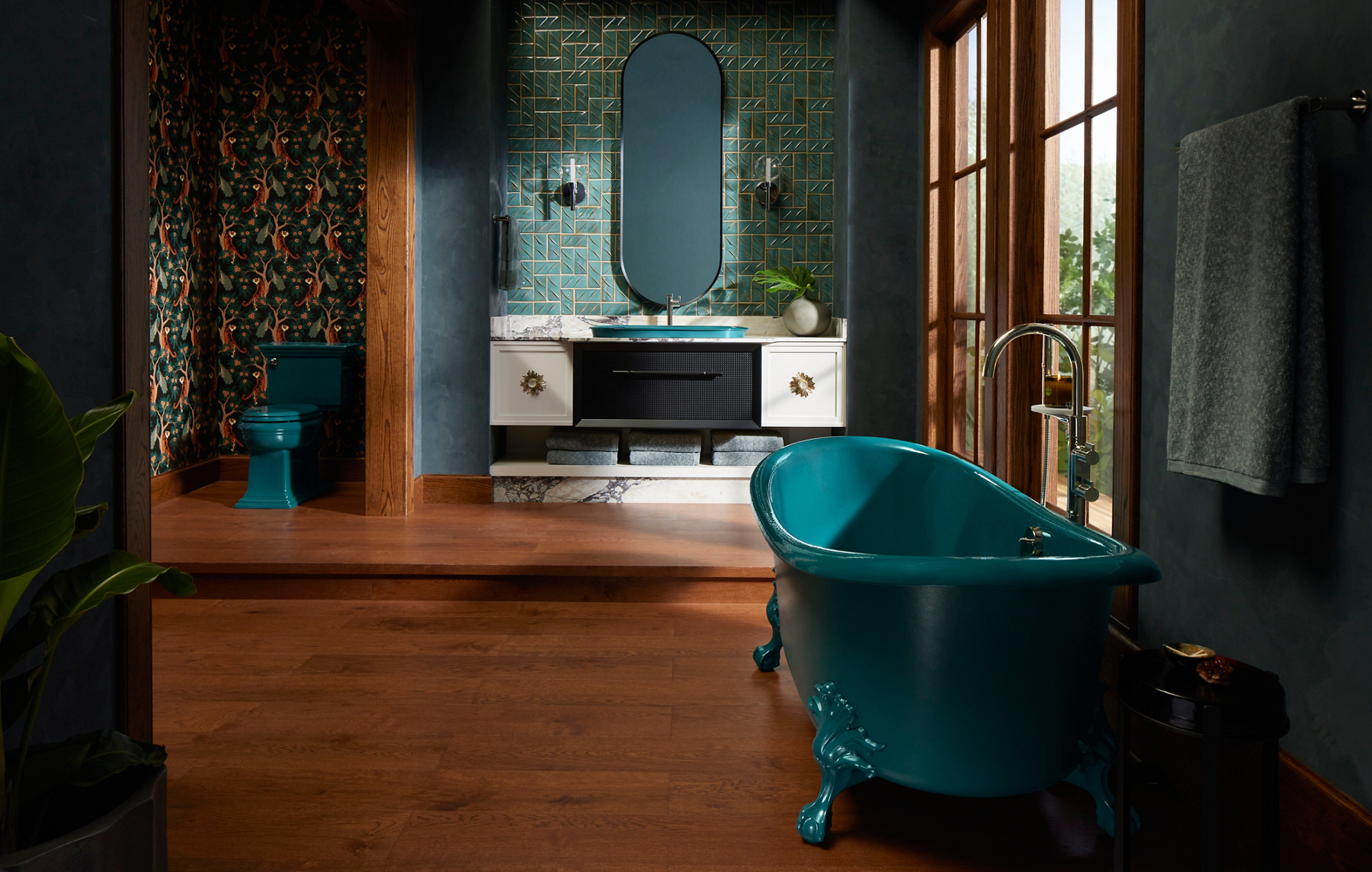 A sunny portrait lifestyle product shot of a teal claw bathtub positioned at a slight angle. The bathtub is made with silver faucets and is surrounded by a tall window at the left, and a towel rack attached to the right side of the wall.