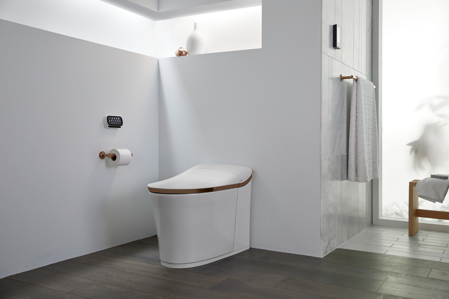 A white KOHLER Eir Intelligent toilet with wall mounted control panel in a bathroom with gray floors and white walls.