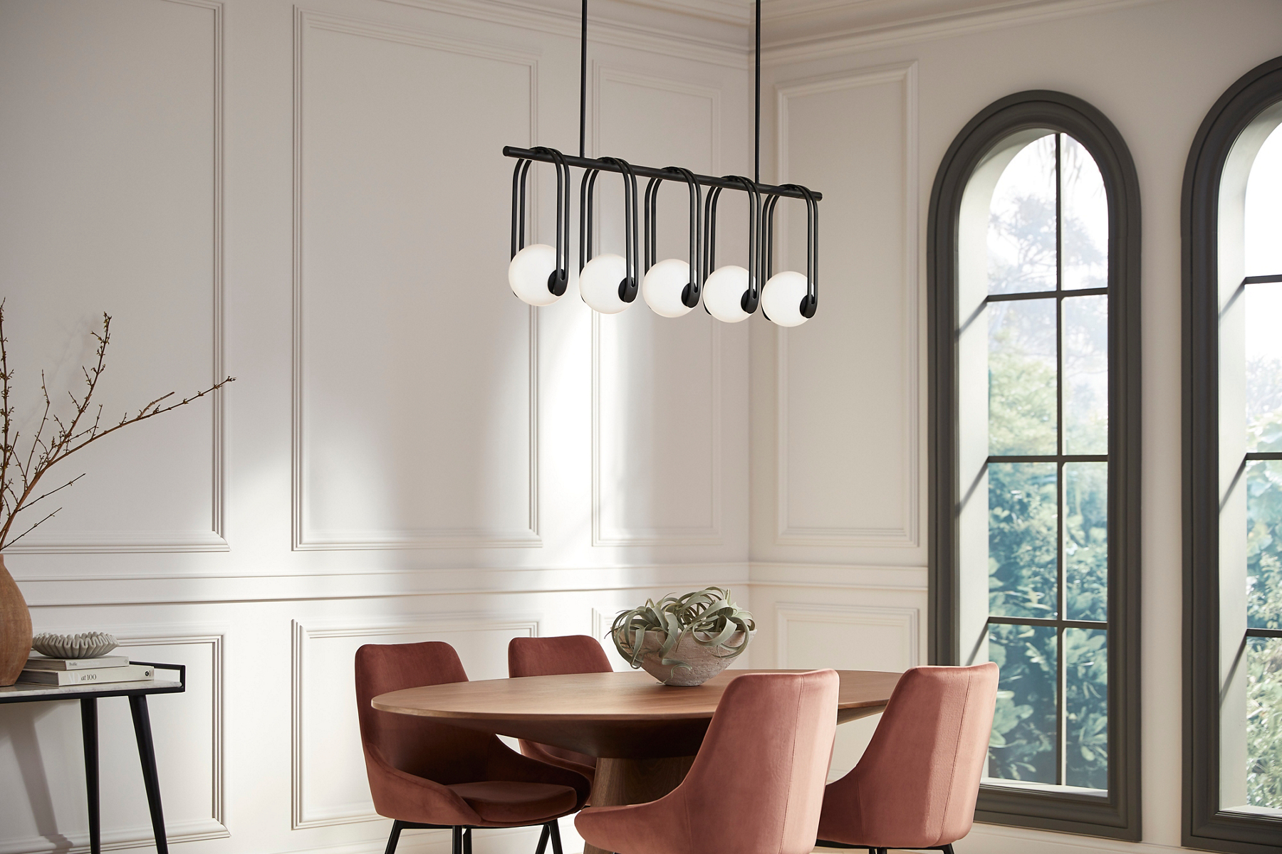 A KOHLER Kraga 5-light chandelier hangs above an oval dining table with a centerpiece of a large bowl of decorative spheres.