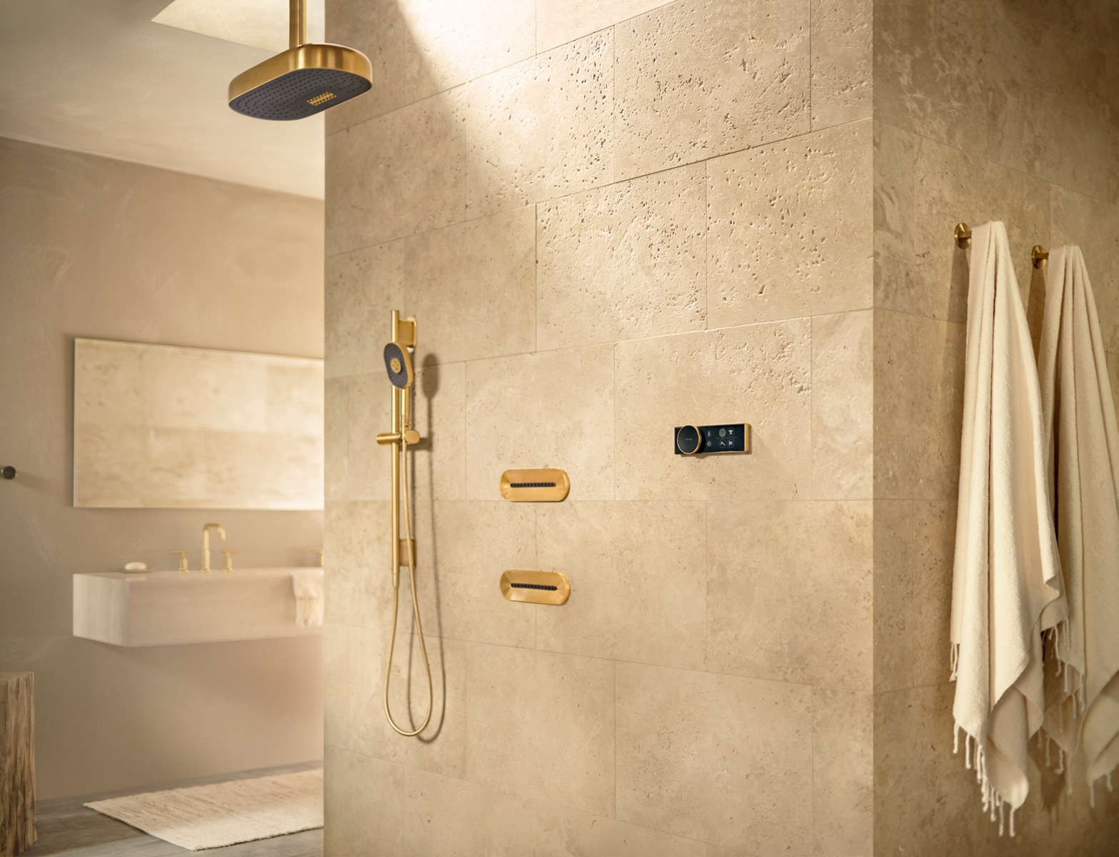 A shower with sand-colored walls, KOHLER Statement rainhead, handshower, and oval body sprays, and an Anthem digital controller.