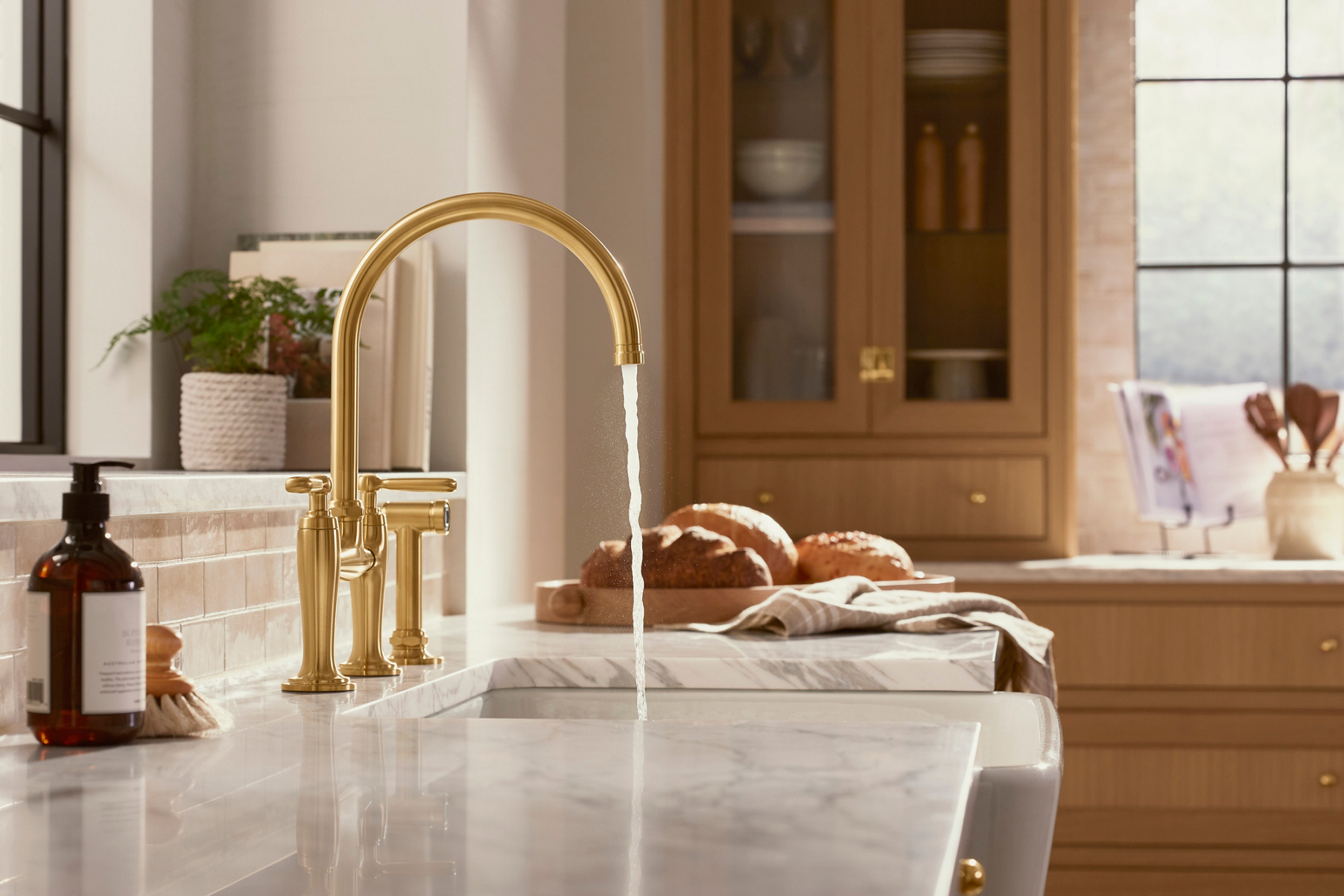 A bridge style faucet with brass finish installed in a kitchen with the water turned on.