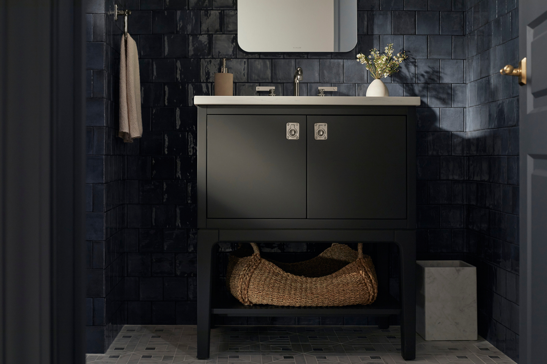 A dark gray vanity, chrome faucet, mirror, and sconce lights designed by Shea McGee in a bathroom with dark blue wall tile.
