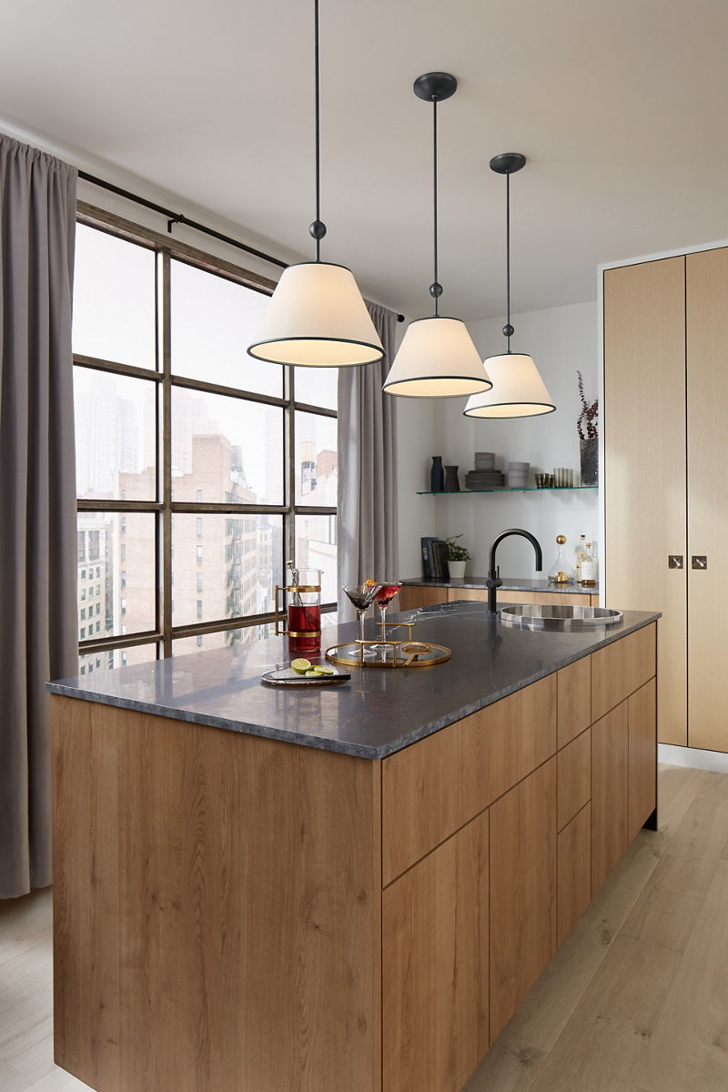 Three pendants with frosted glass shades hang above a kitchen island set for brunch in a kitchen with floor to ceiling windows with city views.